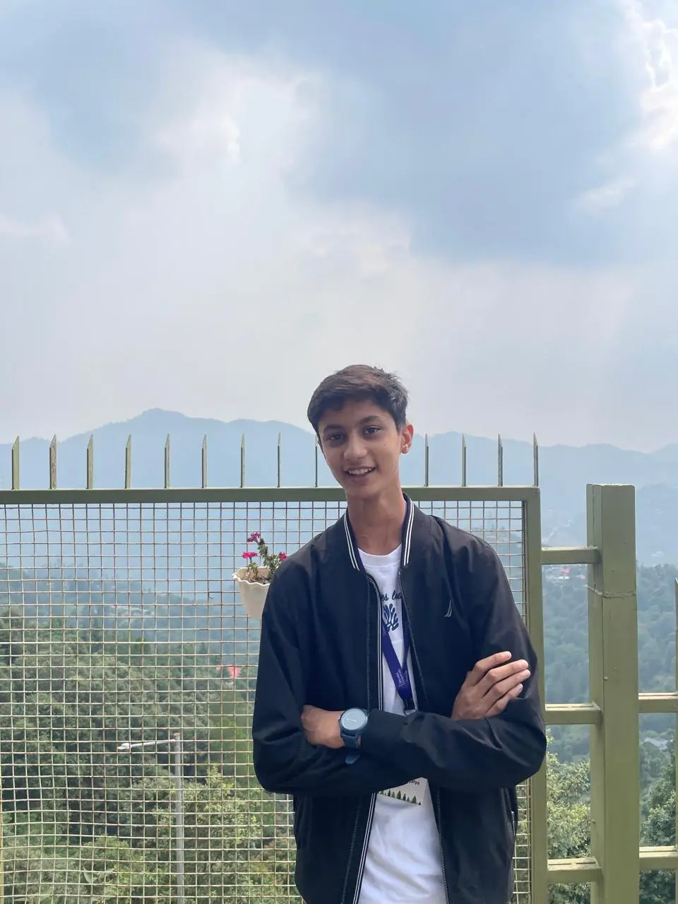 Aaradhy standing with arms crossed by a railing, hills behind